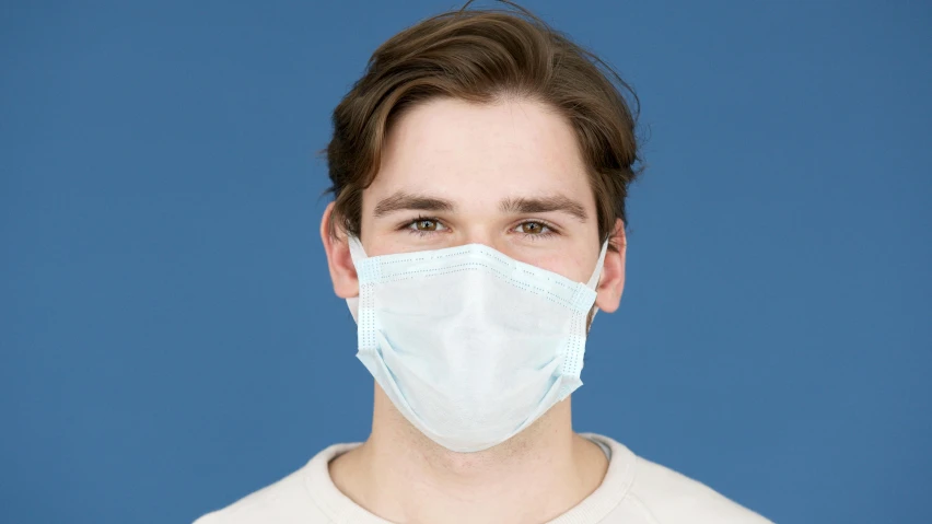 a man wearing a face mask against a blue background, on a pale background, front on, medical image, pretty face