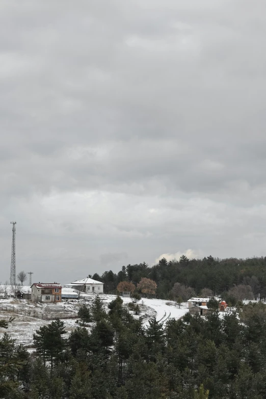 a group of people riding skis on top of a snow covered slope, myllypuro water tower, next to farm fields and trees, with overhead cloudy!!!!! skies, view from a distance