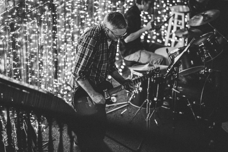 a black and white photo of a man playing a guitar, by Neil Blevins, happening, string lights, steve niles, scott roberston, playing drums