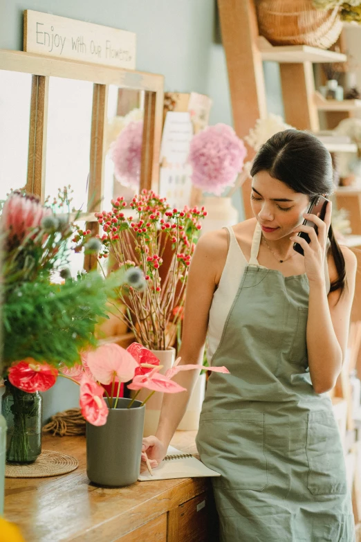 a woman talking on a cell phone in a flower shop, trending on pexels, green and pink colour palette, asian woman, hello, casually dressed