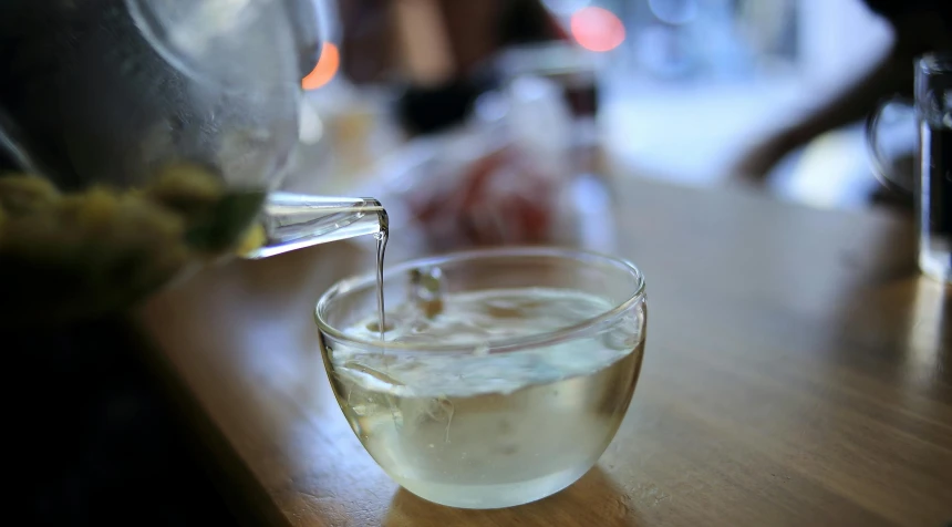 a glass filled with water sitting on top of a wooden table, tea cup, olive oil, on display, pouring