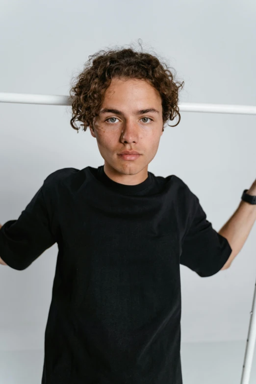 a young man holding a tennis racquet in one hand and a tennis racket in the other, a character portrait, by Jacob Toorenvliet, trending on unsplash, (dark shorter curly hair), frank dillane, wearing black tshirt, crossed arms