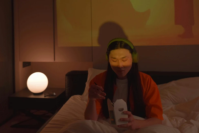 a woman sitting on top of a bed wearing headphones, inspired by Zhang Xiaogang, video art, day - glow facepaint, orange lamp, oled visor over eyes, hotel room