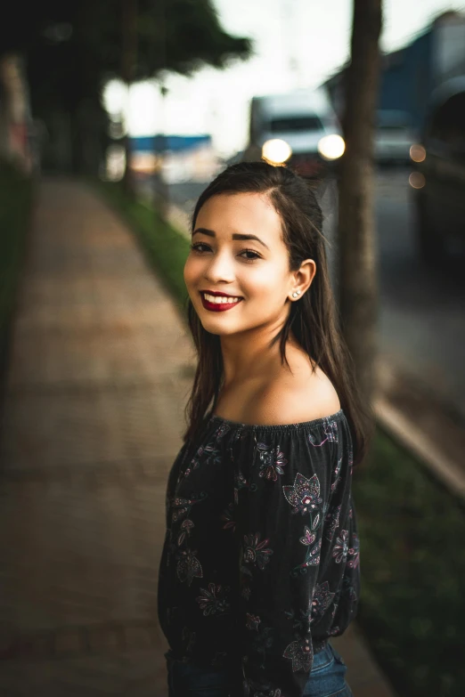 a woman standing on a sidewalk next to a tree, by Reuben Tam, pexels contest winner, realism, smiling young woman, isabela moner, headshot half figure, shoulder-length black hair