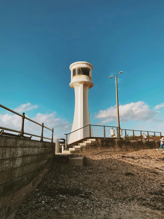 a white lighthouse sitting on top of a sandy beach, an album cover, by Lee Loughridge, unsplash, modernism, lookout tower, maryport, 💋 💄 👠 👗, view from ground level