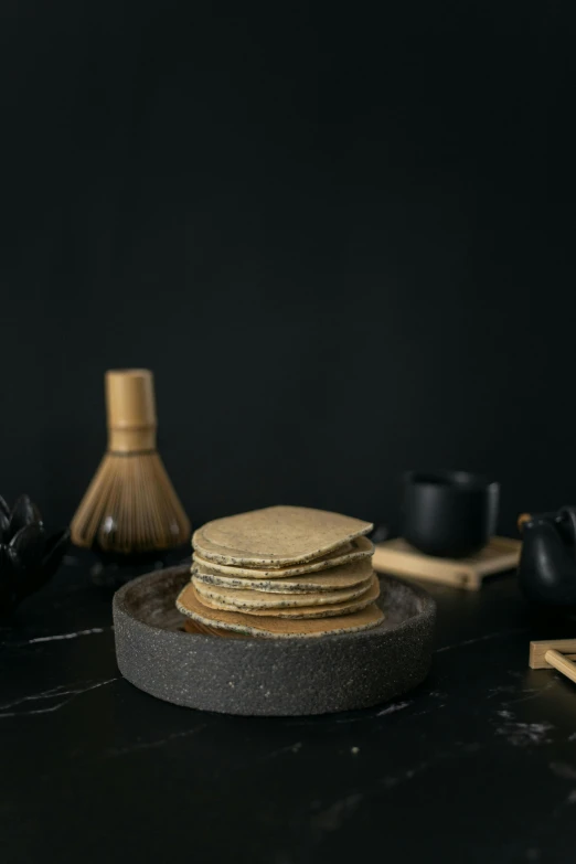 a stack of pancakes sitting on top of a plate, a still life, inspired by Kanō Sanraku, unsplash, renaissance, dark grey, made of bamboo, product view, angled shot
