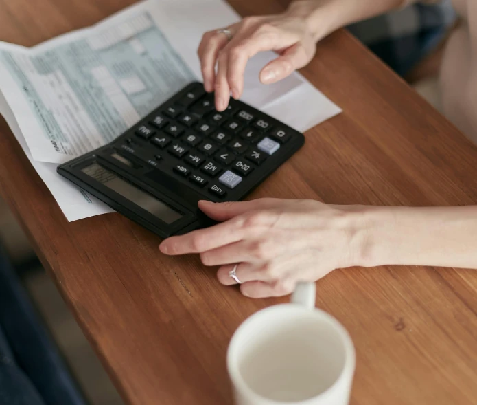 a close up of a person using a calculator, table in front with a cup, lynn skordal, cost, thumbnail