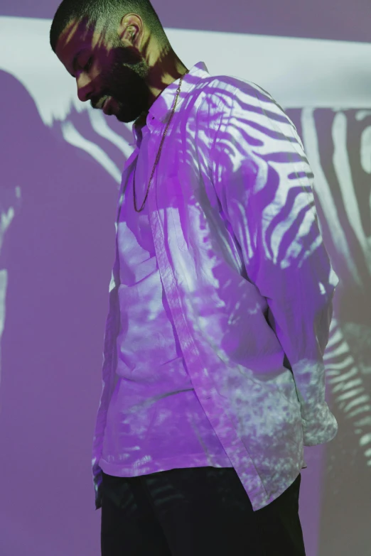 a man standing in front of a projection screen, inspired by Barkley Hendricks, unsplash, holography, purple clothes, back lighting, kanye, in dazzle camouflaged robes