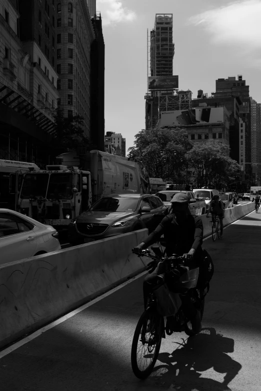 a man riding a motorcycle down a street next to tall buildings, a black and white photo, unsplash, avenida paulista, bicycles, people, manhattan