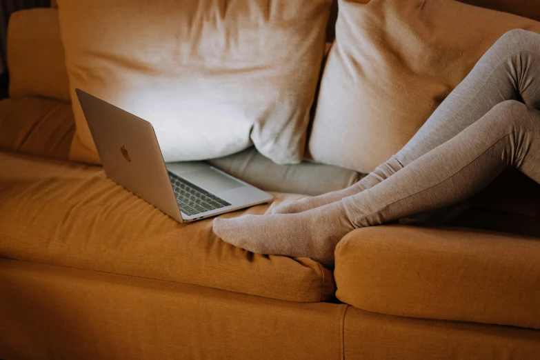 a woman sitting on a couch using a laptop, by Carey Morris, pexels, warm cosy colors, bottom angle, curved furniture, detailed shot legs-up