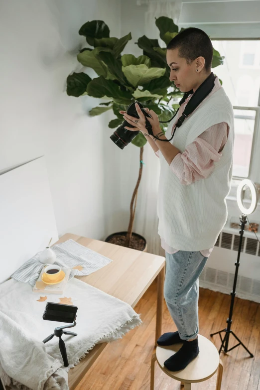 a man standing next to a bed holding a camera, on a white table, plant photography, inspect in inventory image, lighting her with a rim light