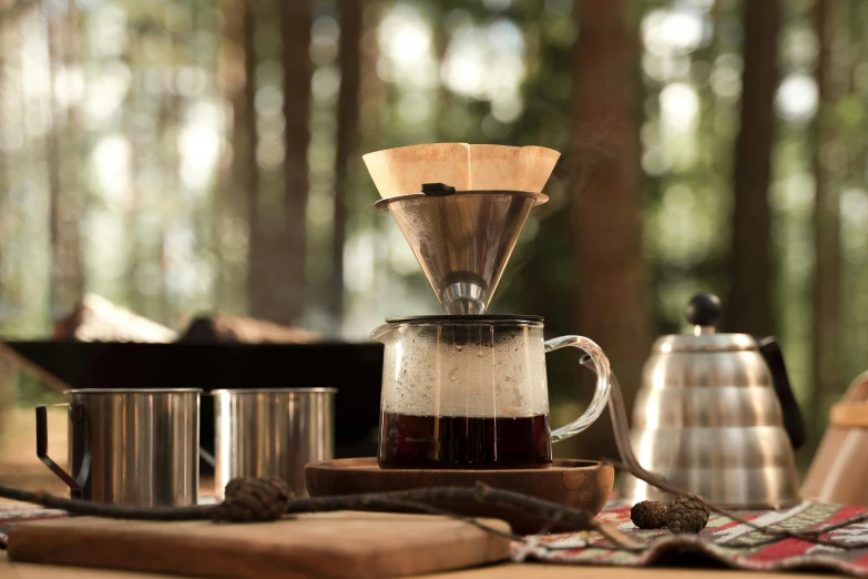 a coffee maker sitting on top of a wooden table, a still life, by Julia Pishtar, hurufiyya, forest picnic, pouring, high quality product image”, close up front view