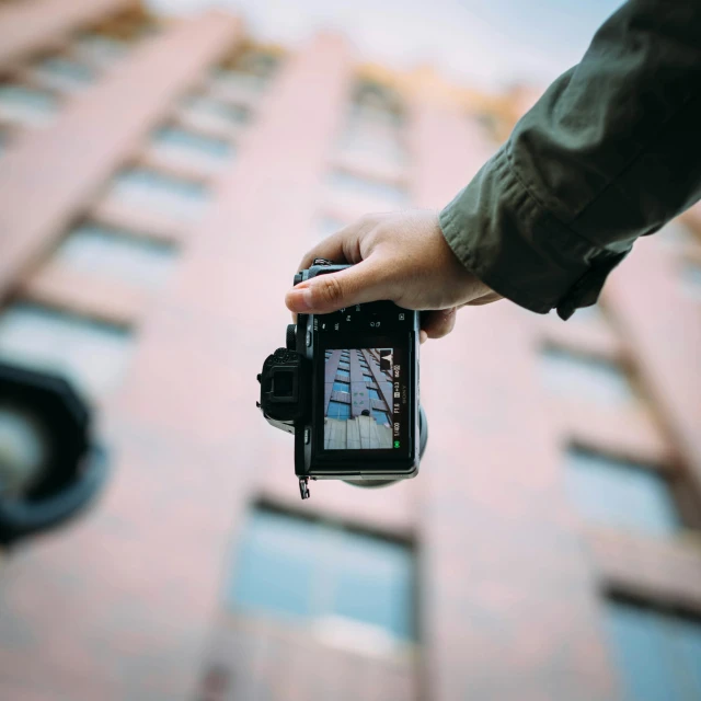 a person holding a camera in front of a tall building, pexels contest winner, sharp focus perfect horizontal, holding it out to the camera, canon eos, home video footage