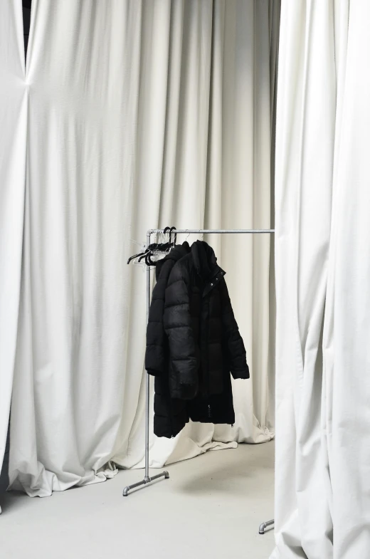a white room with white curtains and a coat on a hanger, by Nina Hamnett, moncler jacket, black coat, backroom background, m