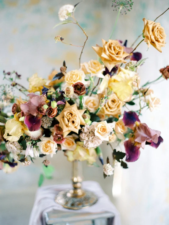 a vase filled with flowers sitting on top of a table, inspired by François Boquet, trending on unsplash, yellow and purple tones, crown of peach roses, exuberant organic elegant forms, ivory and copper