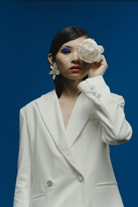 a woman in a white suit holding a seashell, inspired by Ina Wong, aestheticism, wearing a patch over one eye, large opaque blossoms, trench coat and suit, official store photo