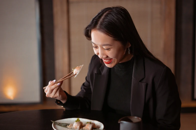 a woman sitting at a table eating sushi, inspired by Miyagawa Chōshun, pexels contest winner, mingei, wearing a turtleneck and jacket, giggling, dumplings on a plate, black