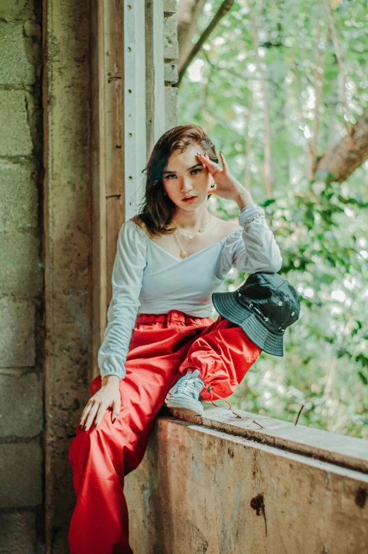 a woman sitting on top of a window sill, a colorized photo, trending on pexels, portrait of modern darna, red cap, pants, cindy avelino