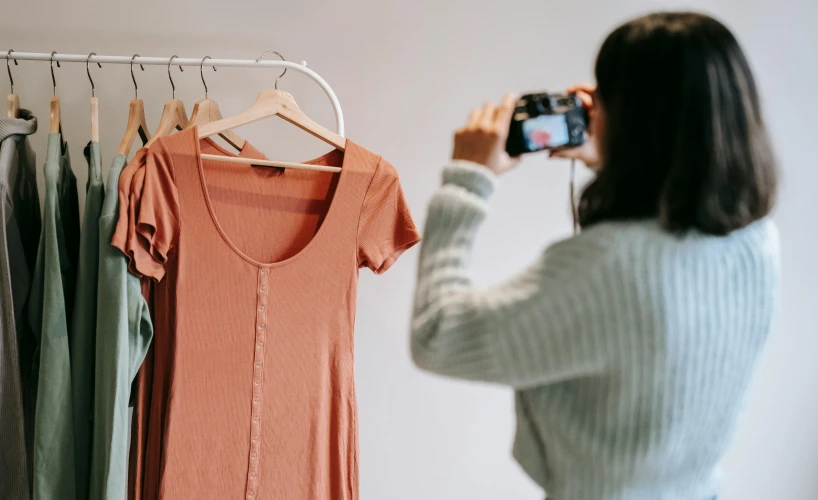 a woman taking a picture of a dress hanging on a rack, trending on pexels, figuration libre, wearing an orange t shirt, studio product shot, 🦩🪐🐞👩🏻🦳, pink clothes