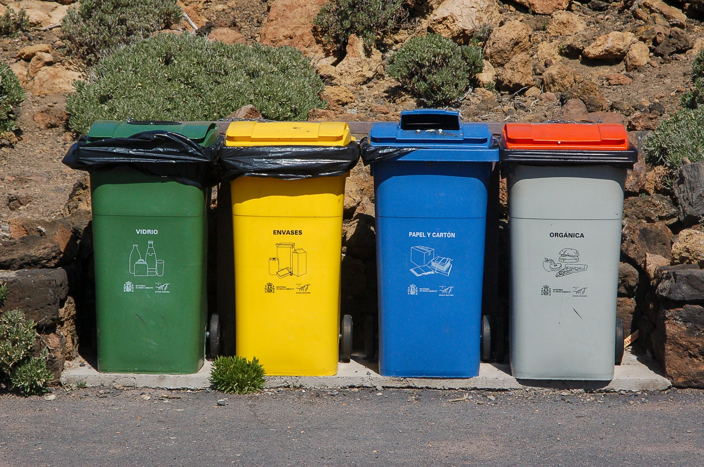 a row of trash cans sitting on the side of a road, a picture, unsplash, plasticien, brand colours are green and blue, hillside, brown, yellow