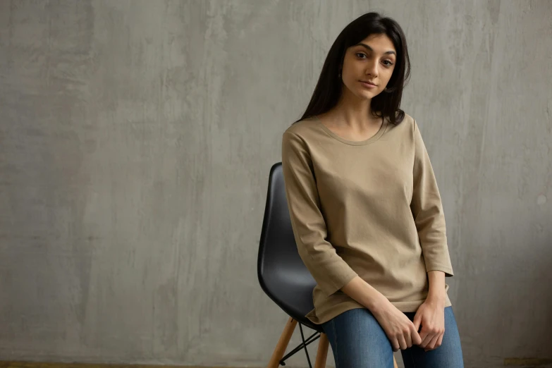 a woman sitting on a chair in a room, inspired by Maggie Hamilton, shutterstock contest winner, wear's beige shirt, sitting on a store shelf, on grey background, dolman