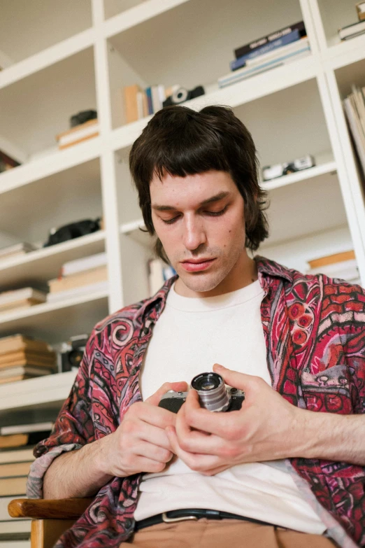 a man sitting in a chair looking at his cell phone, an album cover, by Everett Warner, trending on pexels, nathan fielder, holding a camera, wearing psychedelic wicca, 3 5 mm close up