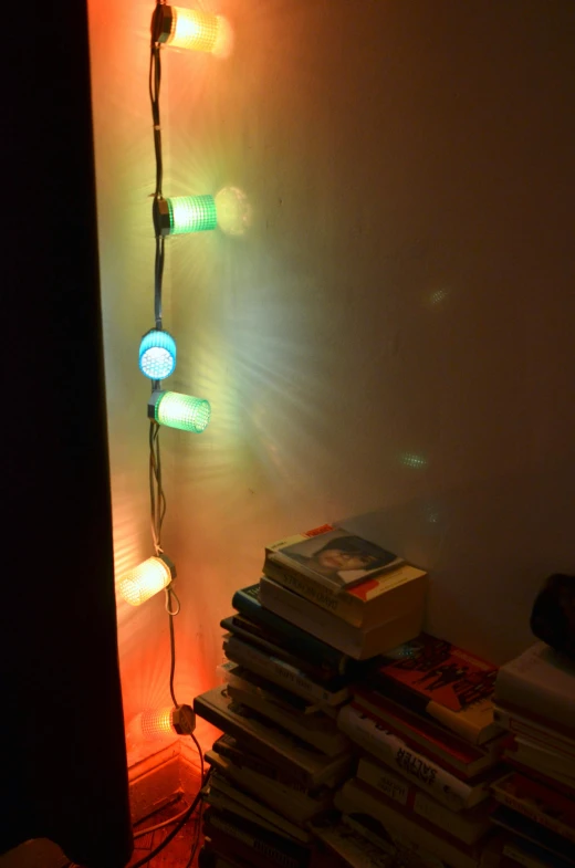 a stack of books sitting on top of a bed next to a lamp, an album cover, inspired by Elsa Bleda, reddit, translucent orbs, glowing lights!!, rgb wall light, made of glowing wax and ceramic