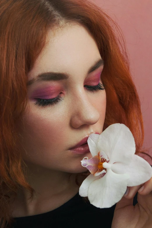 a woman holding a flower in front of her face, an album cover, inspired by Elsa Bleda, trending on pexels, beautiful redhead woman, wearing eye shadow, orchid, pink color palette