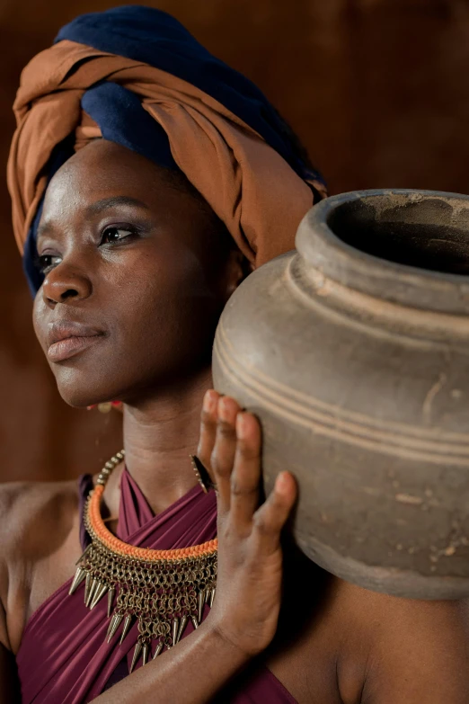 a woman in a turban holding a large pot, by Juan O'Gorman, trending on unsplash, afrofuturism, movie still 8 k, with brown skin, crafts and souvenirs, amphora