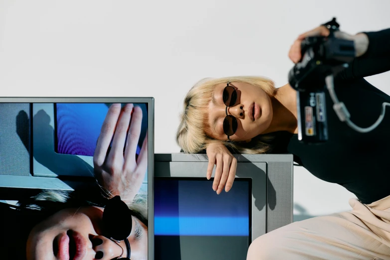 a woman sitting on top of a table next to a tv, by Carey Morris, trending on pexels, video art, futuristic sunglasses, eva elfie, at a fashion shoot, computer screens