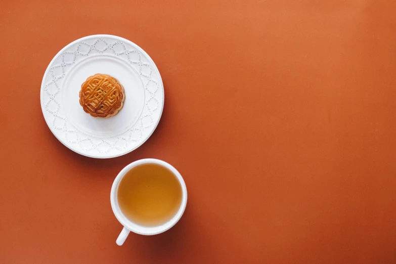 a white plate topped with a pastry next to a cup of tea, inspired by Mi Fu, trending on unsplash, hurufiyya, orange backgorund, square, hong kong, festivals