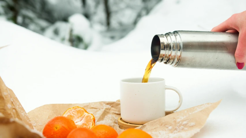 a person pouring orange juice into a cup, by Jakob Gauermann, pexels contest winner, winter in the snow, stainless steel, white mug, thumbnail