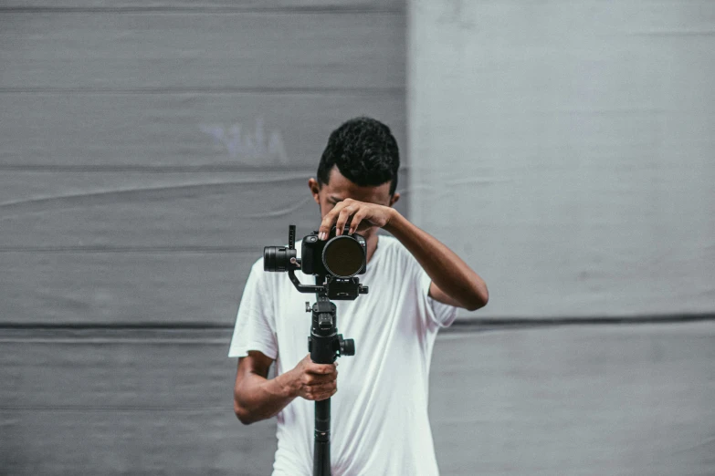 a man holding a camera on top of a tripod, facing the camera