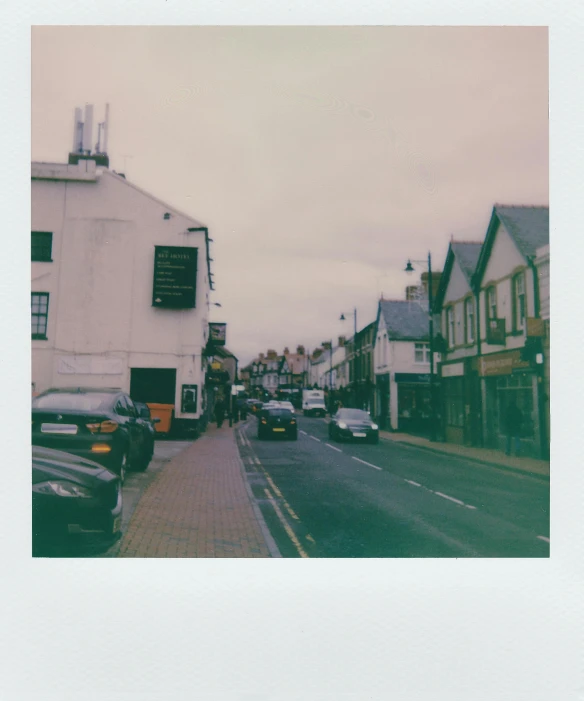 a street with cars parked on the side of it, a polaroid photo, by IAN SPRIGGS, unsplash, small town, polaroid image, wales, medium format