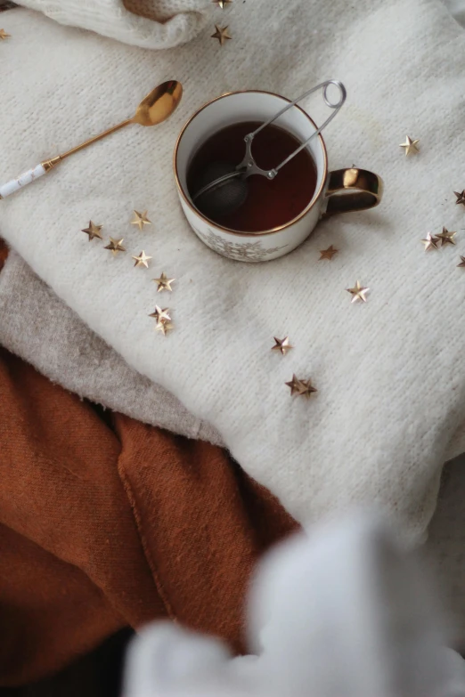 a cup of tea sitting on top of a blanket, by Cosmo Alexander, trending on pexels, aestheticism, tiny stars, brown clothes, thumbnail, ivory and copper