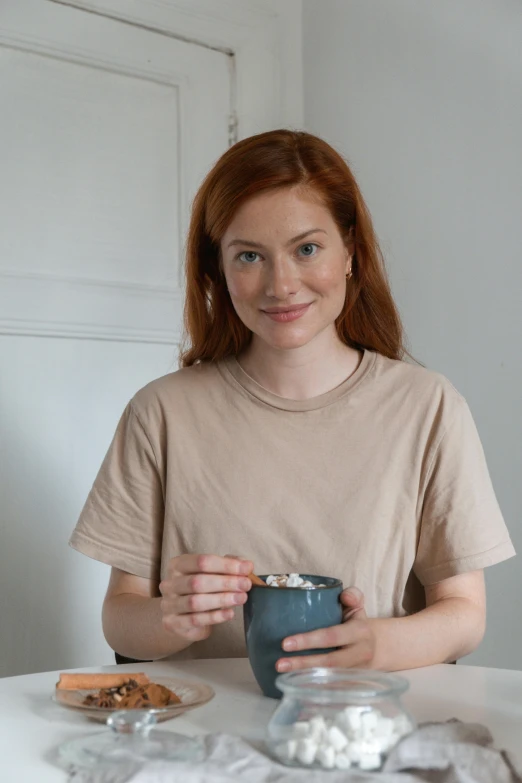 a woman sitting at a table with a cup of coffee, eleanor tomlinson, wearing a t-shirt, detailed product image, hammershøi