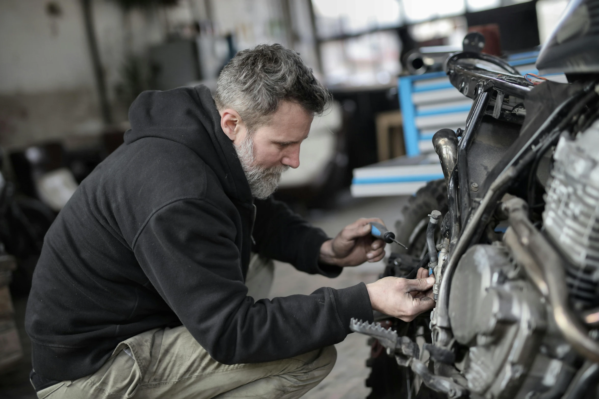 a man working on a motorcycle in a garage, grey, profile image, mechanical - parts, thumbnail