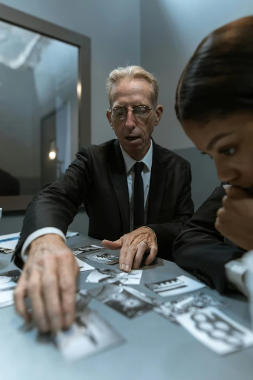 a couple of people that are sitting at a table, an album cover, inspired by Richard Hamilton, pexels contest winner, hyperrealism, in suit with black glasses, in a research facility, imax 7 0 mm. bladerunner, teaching