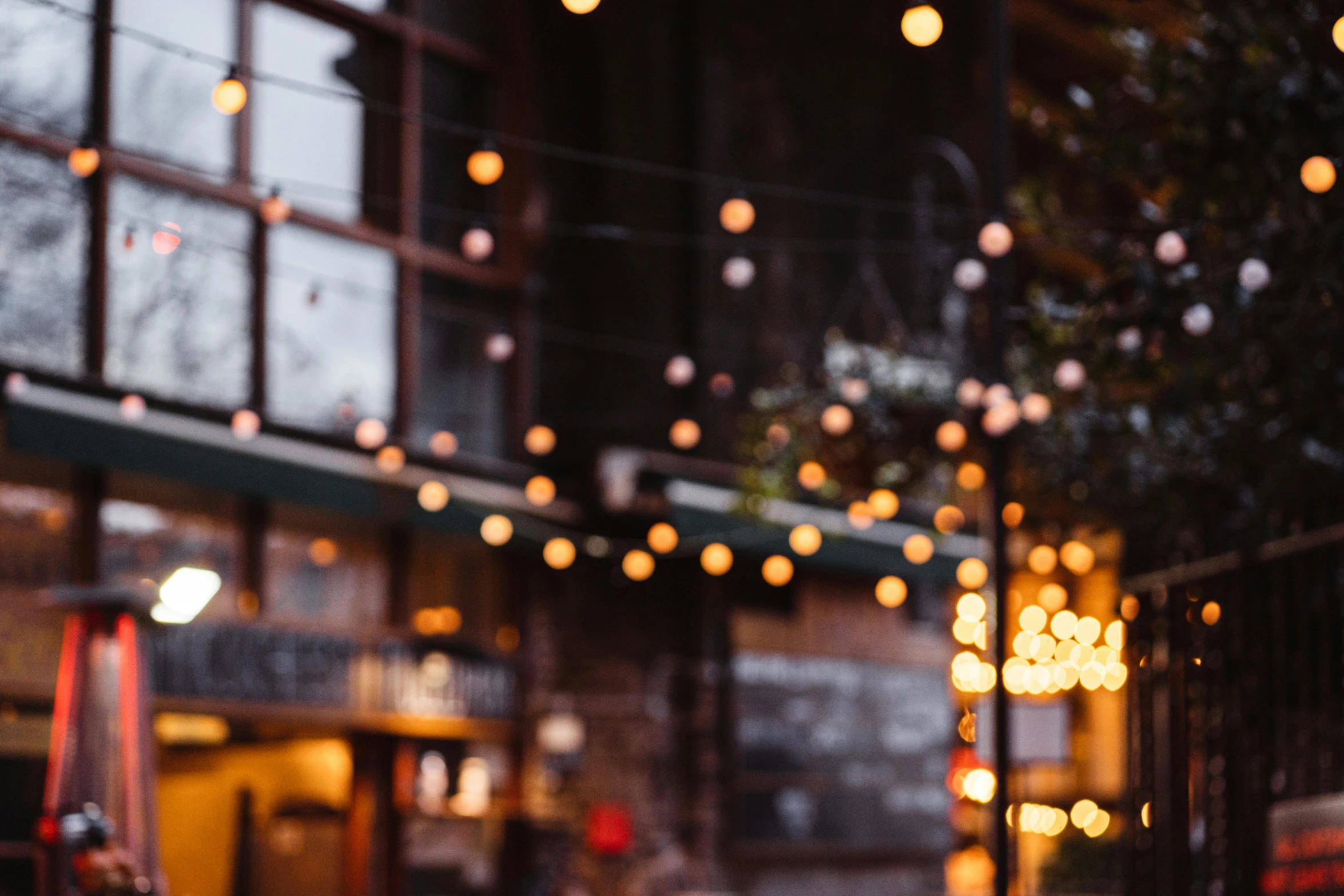 a red fire hydrant sitting on the side of a street, inspired by Elsa Bleda, unsplash contest winner, light and space, candlelit restaurant table, defocused bars in the foreground, hanging lanterns, string lights