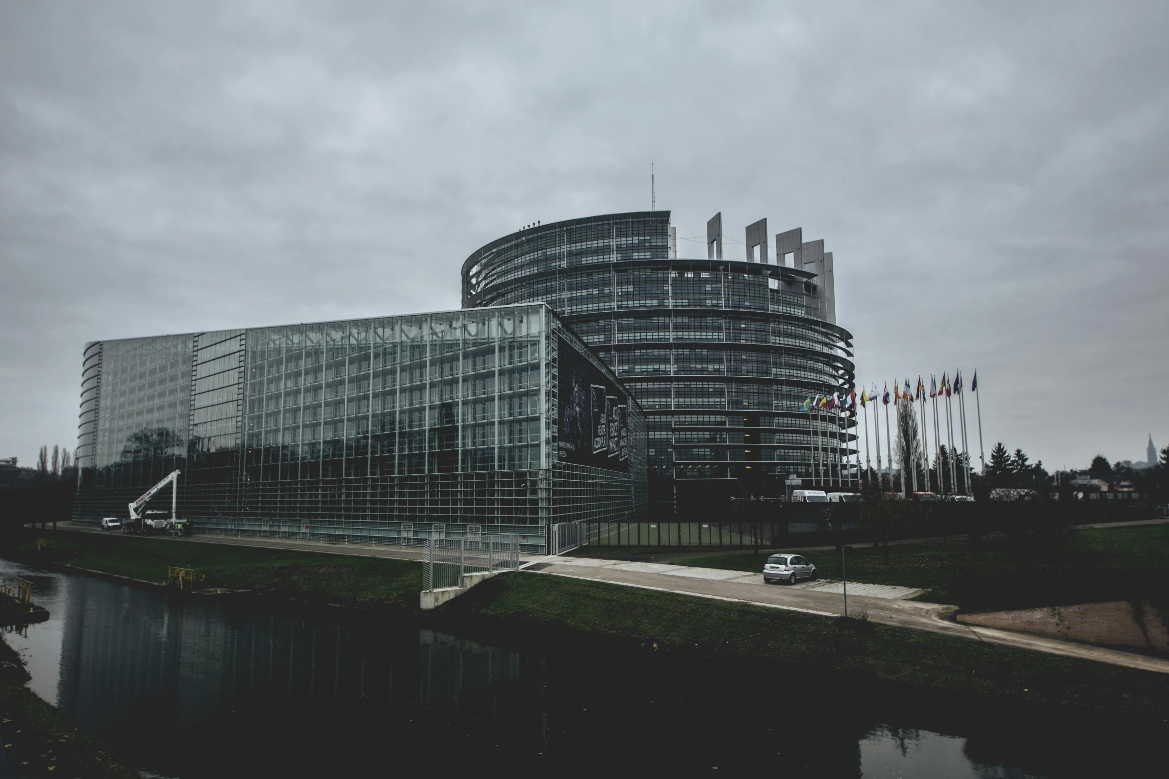 a large building sitting next to a body of water, by Matija Jama, pexels contest winner, brutalism, european union, parliament, gray skies, promo image