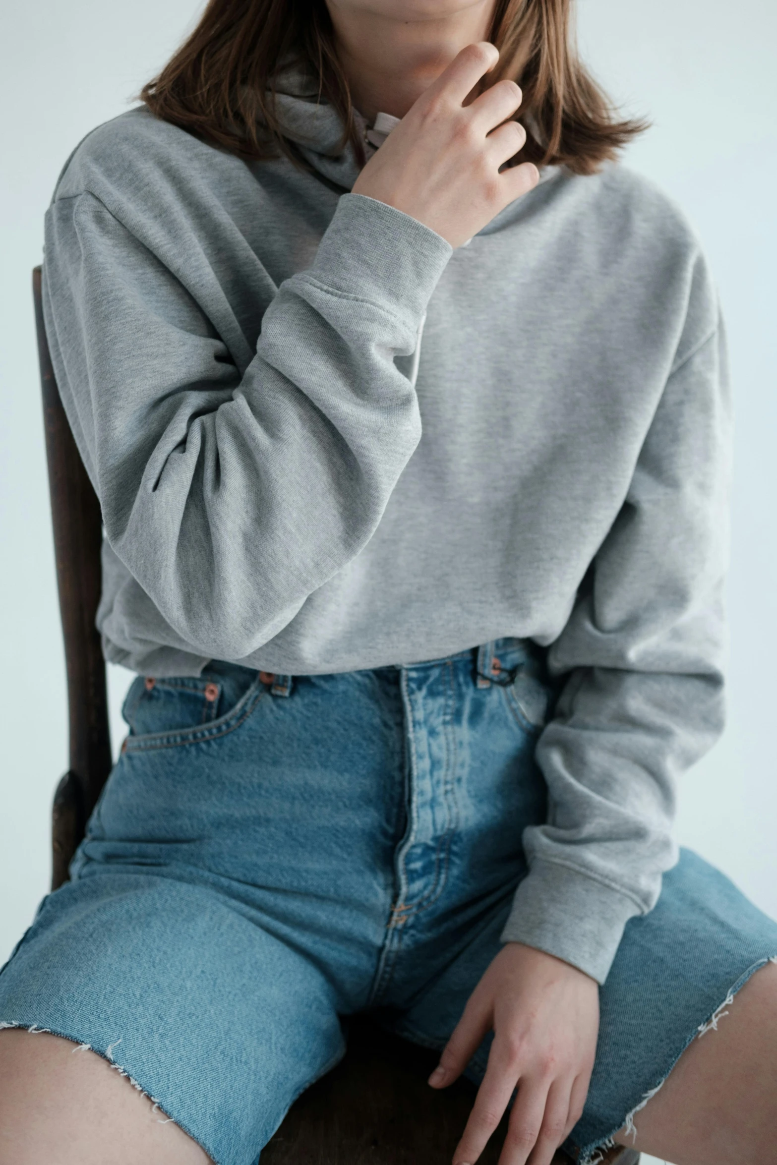 a woman sitting on top of a wooden chair, inspired by Jean Hey, trending on pexels, wearing sweatshirt, light grey, round-cropped, denim
