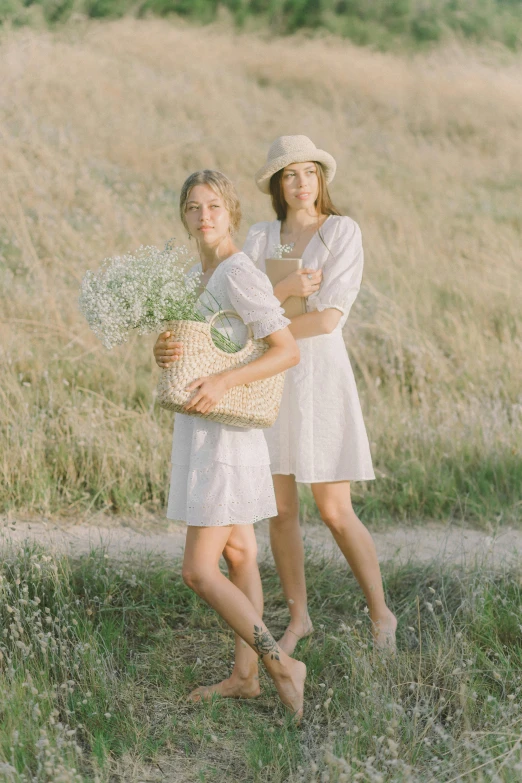 a couple of women standing next to each other in a field, wearing a cute white dress, photoshoot for skincare brand, holding a baguette, trending photo