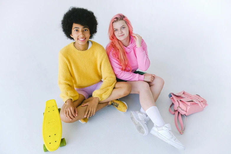 a couple of women sitting on top of a skateboard, trending on pexels, antipodeans, pink and yellow, on a white table, outfit photo, genderless