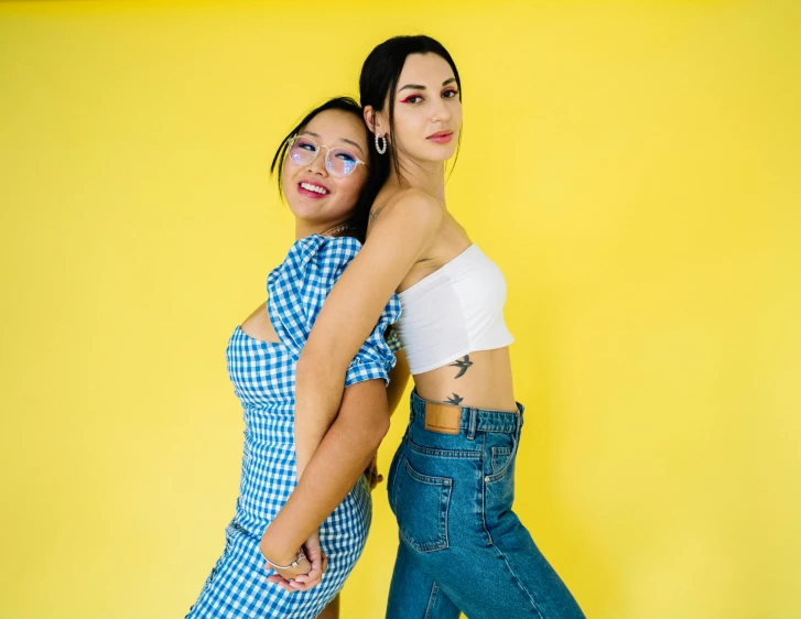 two women standing next to each other in front of a yellow wall, trending on pexels, of taiwanese girl with tattoos, with blue skin, on a checkered floor, arm around her neck