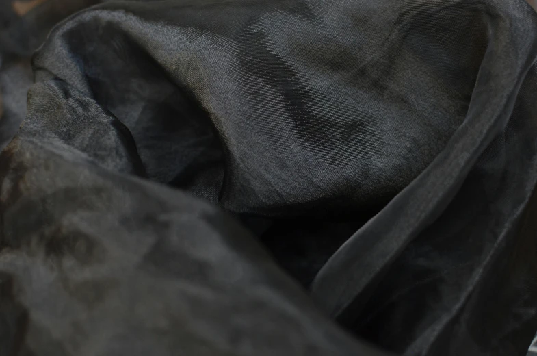 a black bag sitting on top of a wooden floor, a charcoal drawing, by Helen Stevenson, unsplash, baroque, soft translucent fabric folds, detail texture, black jacket | shiny, zoomed in