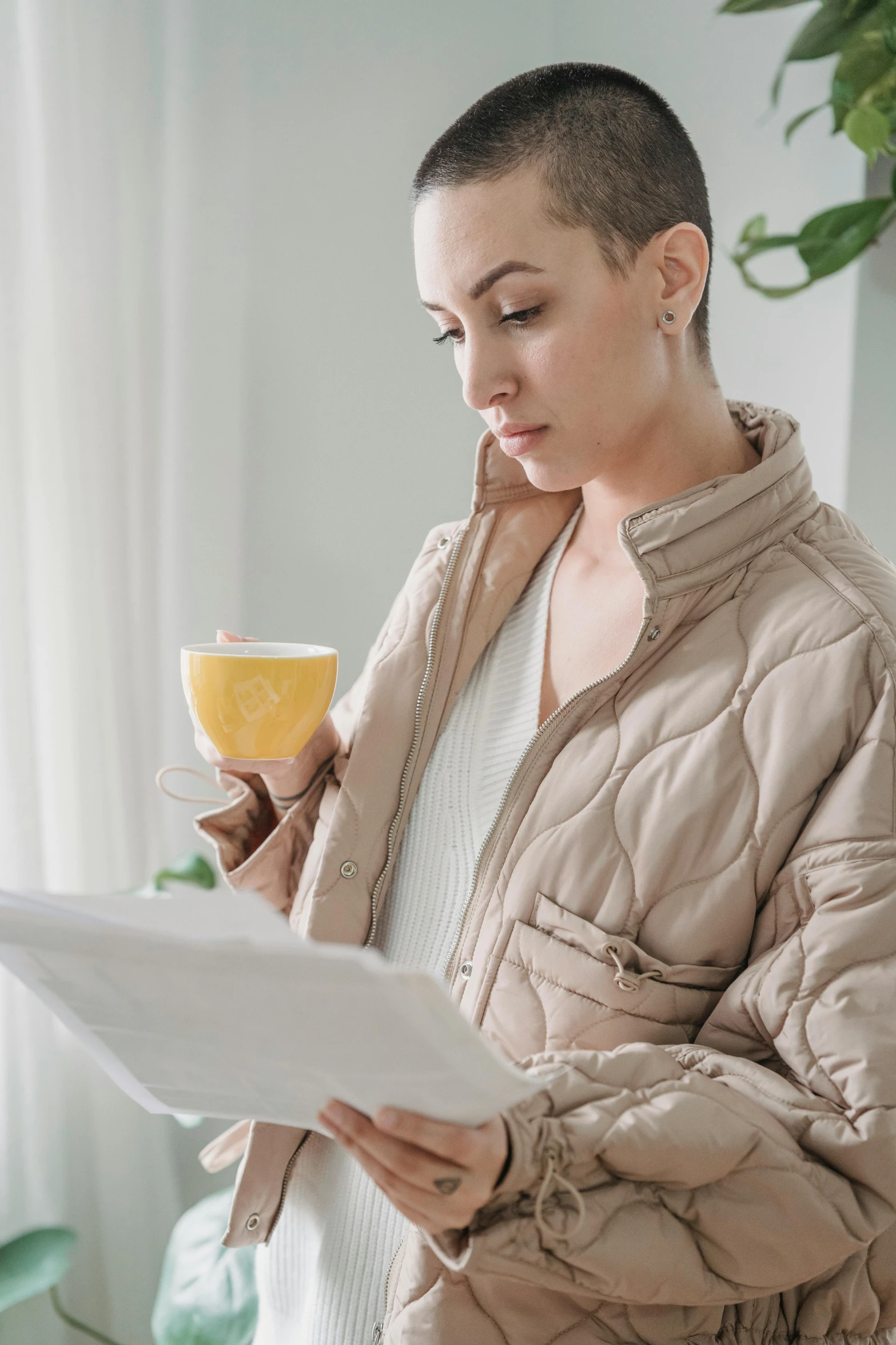 a woman reading a piece of paper while holding a cup of coffee, model wears a puffer jacket, wearing wheat yellow gauze, profile image, wearing a track suit