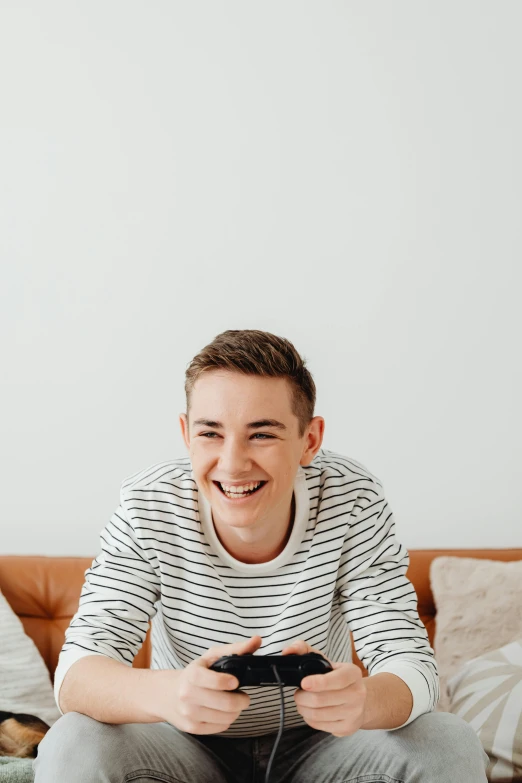 a man sitting on a couch playing a video game, by Cosmo Alexander, trending on pexels, wearing stripe shirt, happily smiling at the camera, declan mckenna, headshot profile picture
