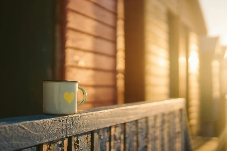 a coffee cup sitting on top of a wooden bench, inspired by Elsa Bleda, pexels contest winner, romanticism, golden hour 8 k, balcony, yellow, medium format. soft light