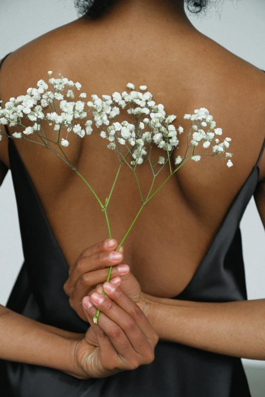 a woman in a black dress holding a bunch of flowers, inspired by Robert Mapplethorpe, ebony skin, gypsophila, back slit, skincare