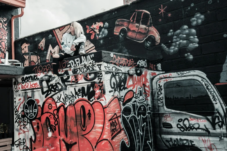 a truck parked in front of a building covered in graffiti, pexels contest winner, graffiti, girl sitting on a rooftop, red and white and black colors, thumbnail, background image
